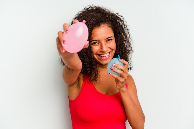 Young Brazilian woman holding water balloons isolated on blue background