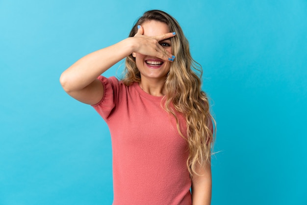 Young Brazilian woman isolated on blue background covering eyes by hands and smiling