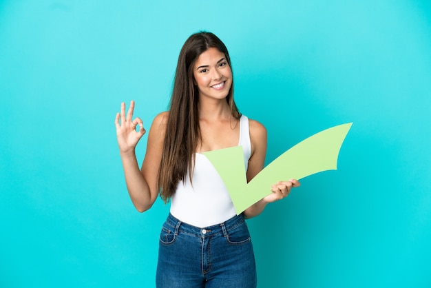 Young brazilian woman isolated on blue background holding a\
check icon and doing ok sign