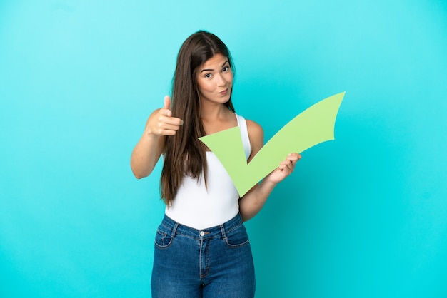 Young Brazilian woman isolated on blue background holding a check icon and pointing to the front