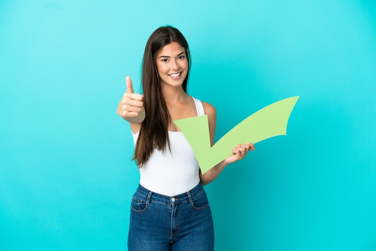 Photo young brazilian woman isolated on blue background holding a check icon with thumb up