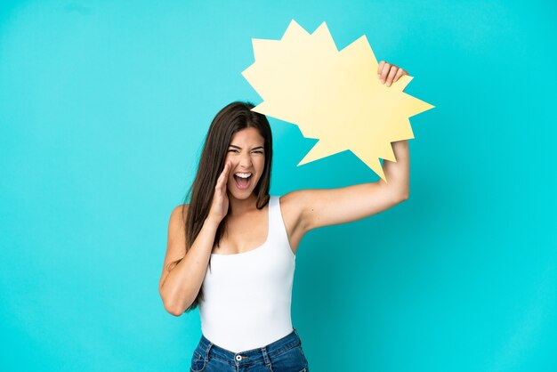 Young Brazilian woman isolated on blue background holding an empty speech bubble and shouting