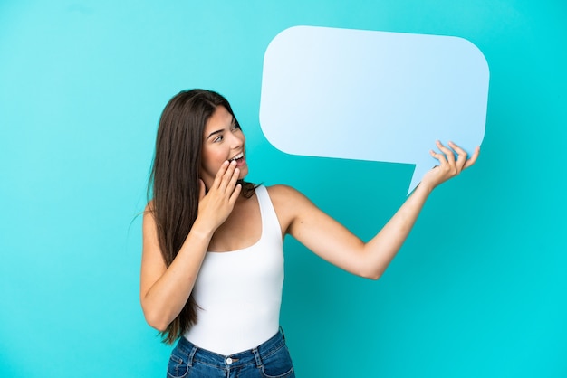 Young Brazilian woman isolated on blue background holding an empty speech bubble with surprised expression