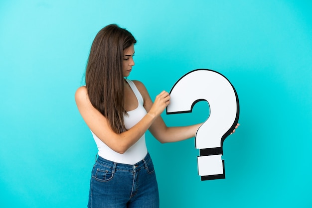 Young Brazilian woman isolated on blue background holding a question mark icon