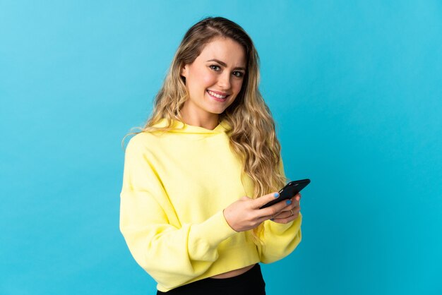 Young Brazilian woman isolated on blue background sending a message with the mobile