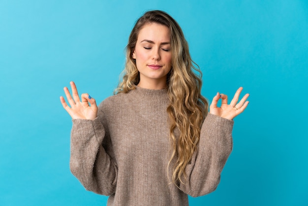 Young Brazilian woman isolated on blue in zen pose