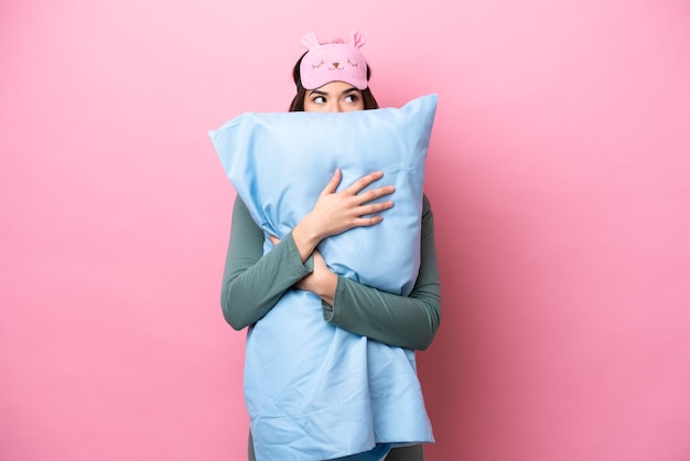 Photo young brazilian woman isolated on pink background in pajamas and holding a pillow