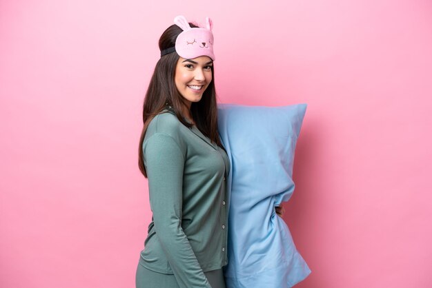 Photo young brazilian woman isolated on pink background in pajamas and smiling a lot