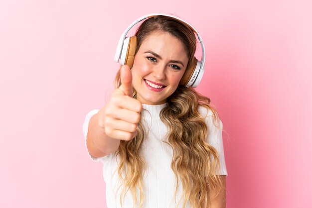Young brazilian woman isolated on pink listening music and with thumb up
