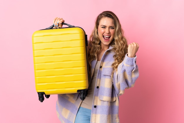 Young Brazilian woman isolated on pink  in vacation with travel suitcase