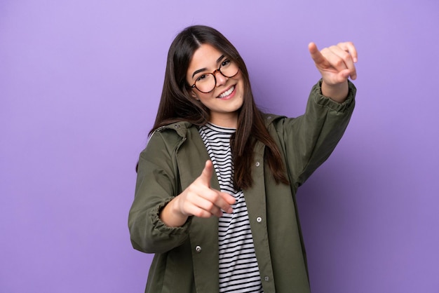 Young brazilian woman isolated on purple background pointing front with happy expression