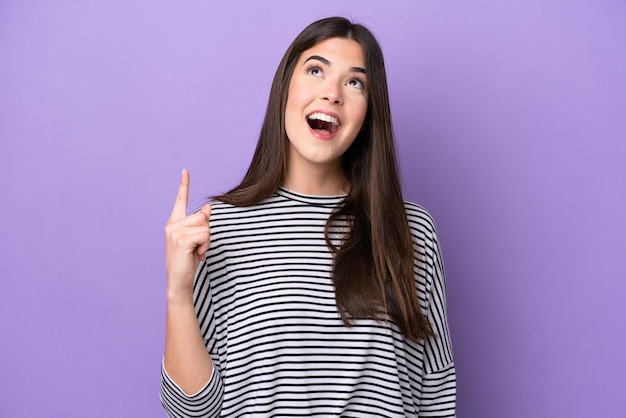 Young Brazilian woman isolated on purple background pointing up and surprised