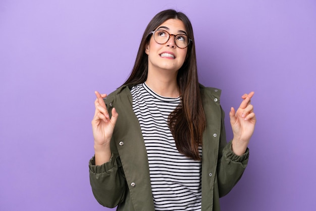 Young brazilian woman isolated on purple background with fingers crossing and wishing the best