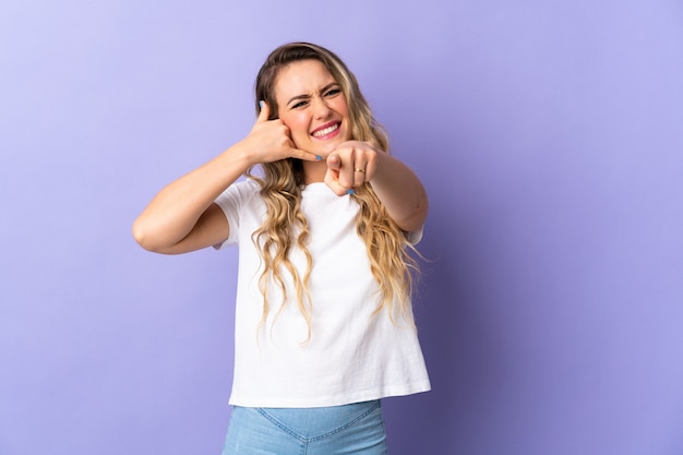 Young Brazilian woman isolated on purple  making phone gesture and pointing front