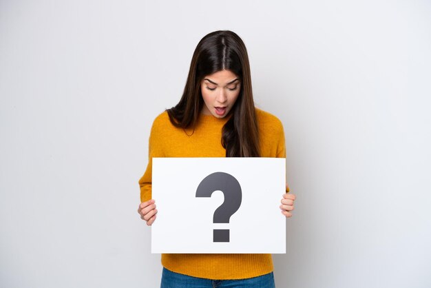 Young Brazilian woman isolated on white background holding a placard with question mark symbol