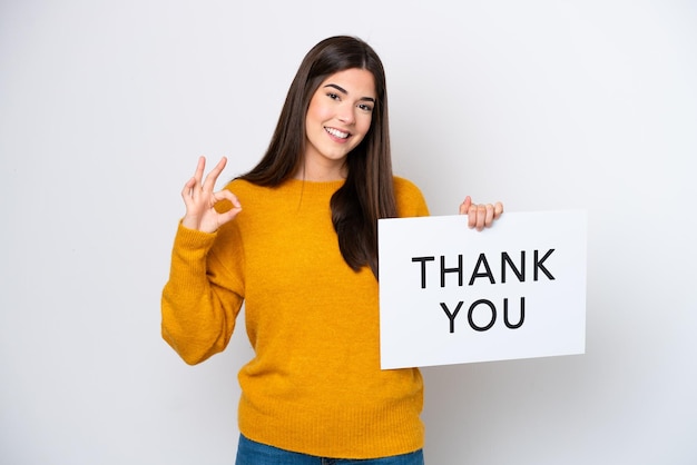 Photo young brazilian woman isolated on white background holding a placard with text thank you with ok sign