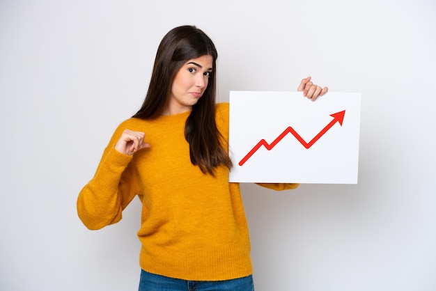 Young brazilian woman isolated on white background holding a sign with a growing statistics arrow symbol with proud gesture