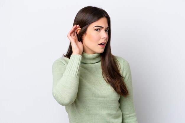 Young Brazilian woman isolated on white background listening to something by putting hand on the ear