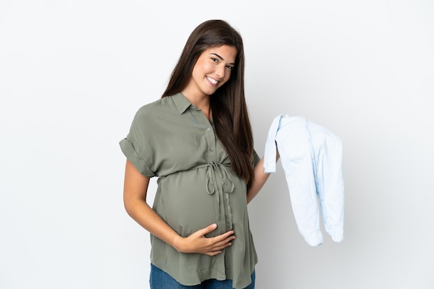 Young Brazilian woman isolated on white background pregnant and holding baby clothes