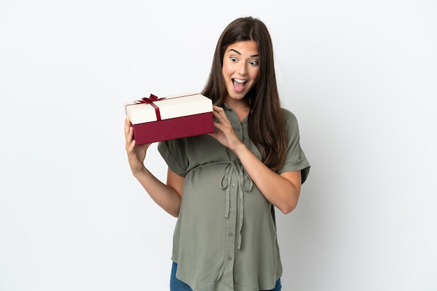 Young Brazilian woman isolated on white background pregnant and holding a gift with surprised expression