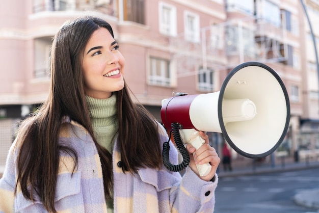 Young Brazilian woman at outdoors holding a megaphone and looking up while smiling