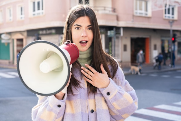 Young Brazilian woman at outdoors shouting through a megaphone with surprised expression