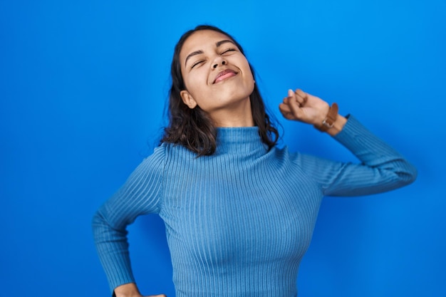 Young brazilian woman standing over blue isolated background stretching back, tired and relaxed, sleepy and yawning for early morning