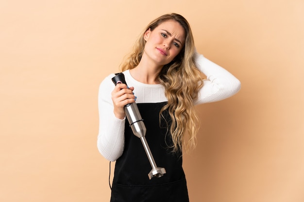 Young brazilian woman using hand blender isolated on beige having doubts