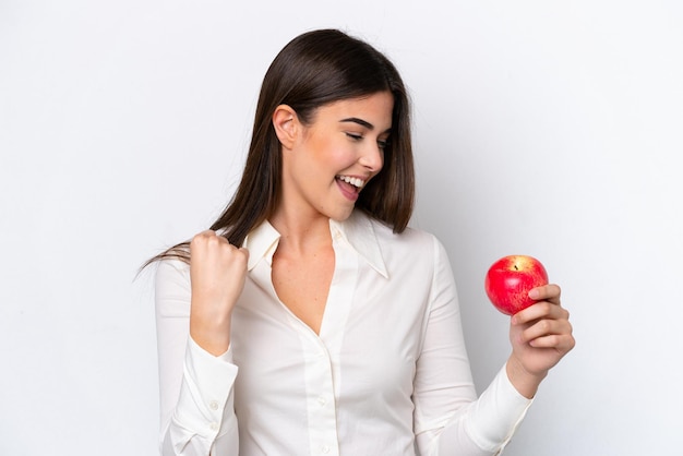 Young Brazilian woman with an apple isolated on white background celebrating a victory