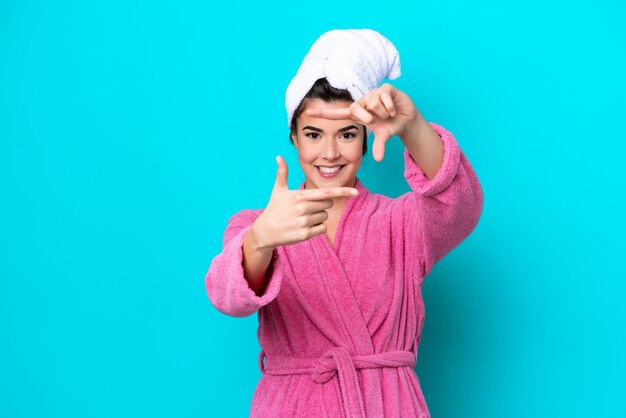 Young Brazilian woman with a bathrobe isolated on blue background focusing face Framing symbol