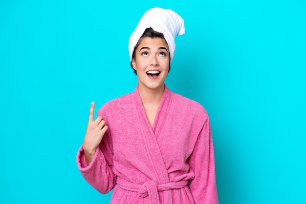 Young Brazilian woman with a bathrobe isolated on blue background pointing up and surprised