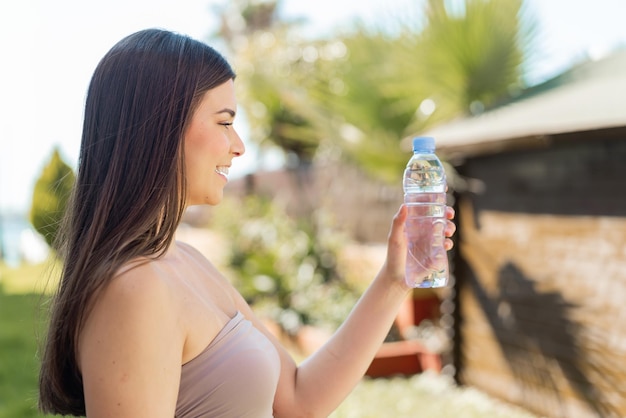 Photo young brazilian woman with a bottle of water at outdoors with happy expression