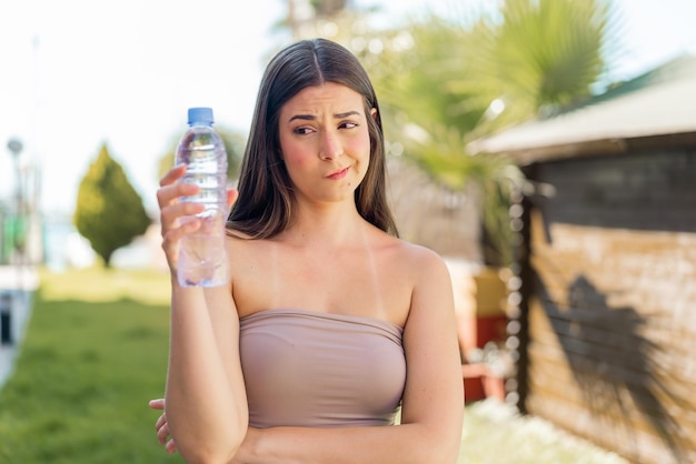 Young Brazilian woman with a bottle of water at outdoors with sad expression