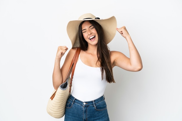 Young Brazilian woman with Pamela holding a beach bag isolated on white background celebrating a victory