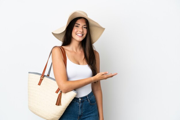 Young Brazilian woman with Pamela holding a beach bag isolated on white background presenting an idea while looking smiling towards