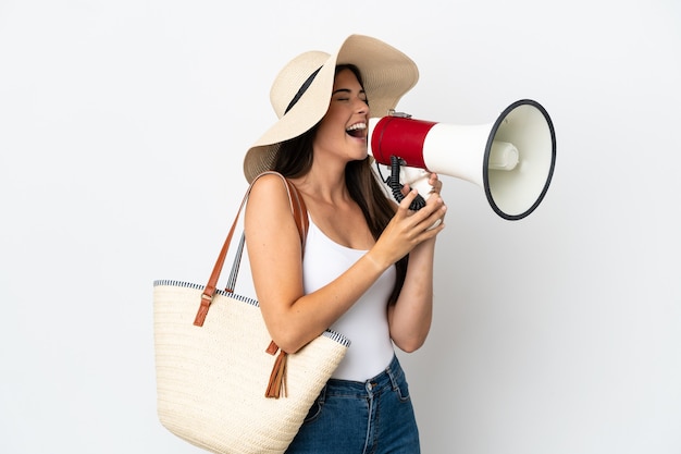 Young Brazilian woman with Pamela holding a beach bag isolated on white background shouting through a megaphone