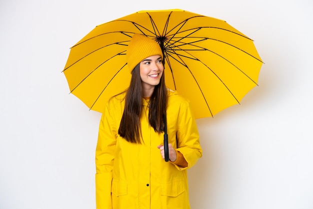 Young Brazilian woman with rainproof coat and umbrella isolated on white background looking side