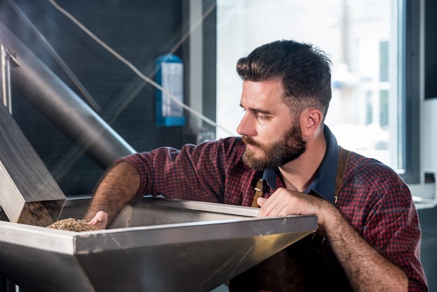 Photo a young brewer in a leather apron controls the grinding of malt seeds in a mill at a modern brewery