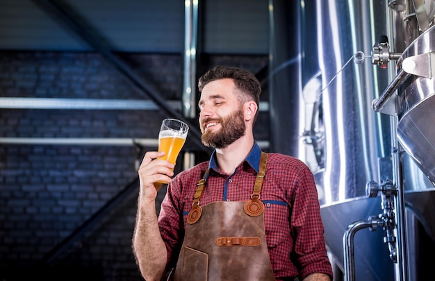 Photo young brewer wearing a leather apron is testing beer at a modern brewery