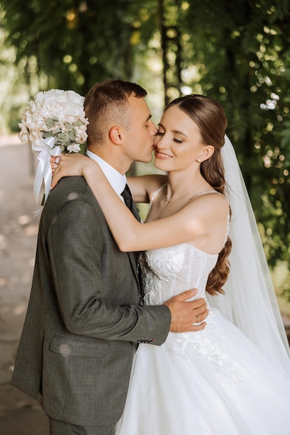 A young bride and groom tenderly embrace in the rays of the autumn sun Tender and beautiful young girl bride A man kisses his beloved Against the background of a beautiful garden