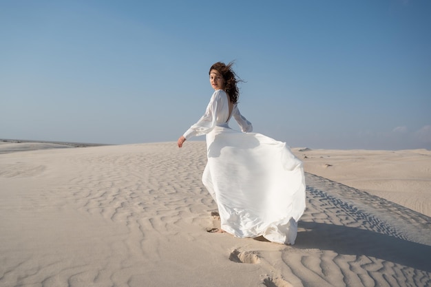 Young bride in white waving gown walking a a sand dune in desert