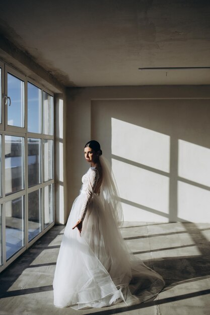 Young bride in white wedding dress holding bouquet and looking away at home