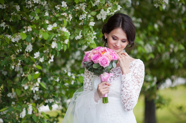 Young bride with pink wedding bouquet in blooming garden