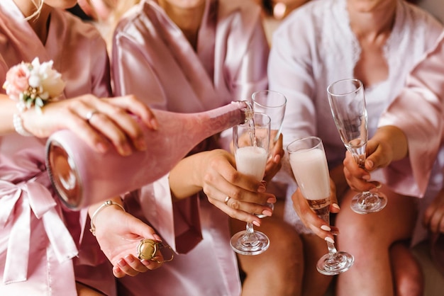 Photo young bridesmaids clinking with glasses of champagne in hotel room closeup photo of cheerful girls celebrating a bachelorette party females have toast with wine