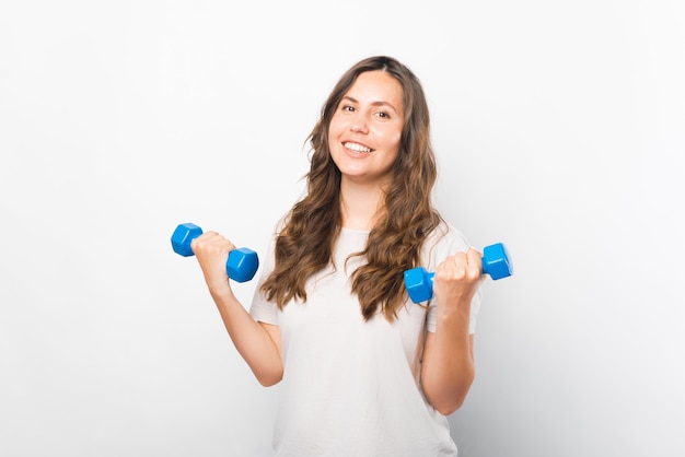 Young bright girl is lifting up two dumbbells over white background.