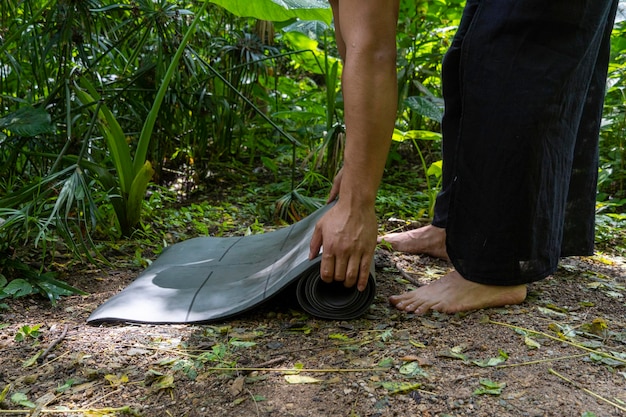 Young brown latin man rolling up his mat to exercise in the forest surrounded by vegetation mexico l