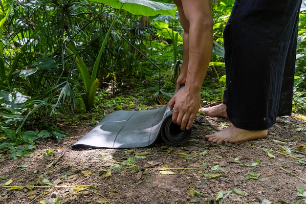 Young brown latin man rolling up his mat to exercise in the forest surrounded by vegetation mexico