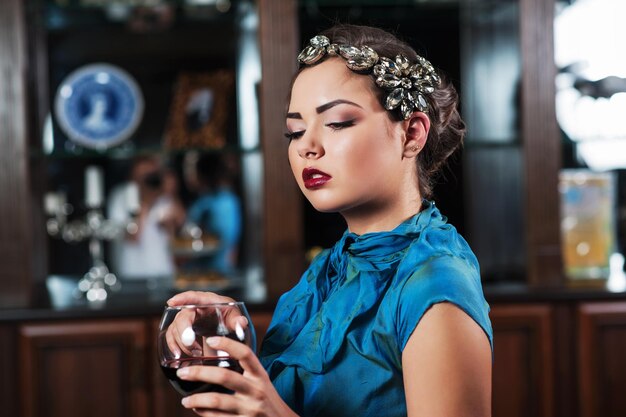 La giovane ragazza dai capelli castani sta bevendo e assaggiando un bicchiere di vino rosso secco