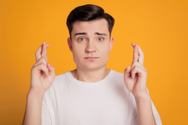 Young brunet man keep fingers crossed isolated over yellow background