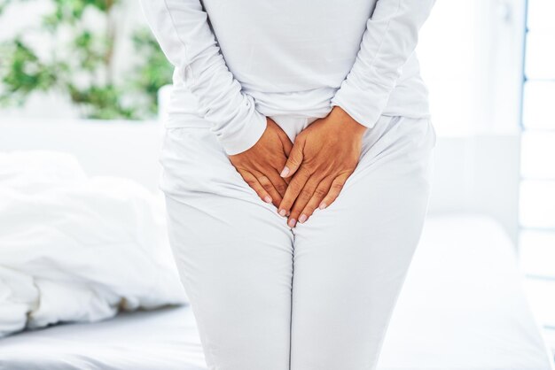 Young brunet woman with menstrual pain over bright bed